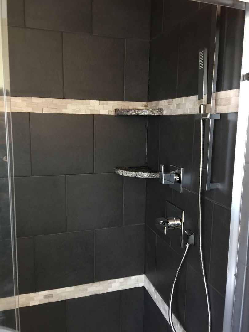 Black tiled shower with chrome fixtures and glass door.