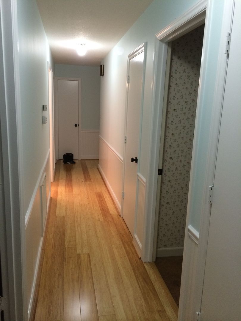 Hallway with light blue walls, wood floor, and white trim. Open door to room with patterned wallpaper.