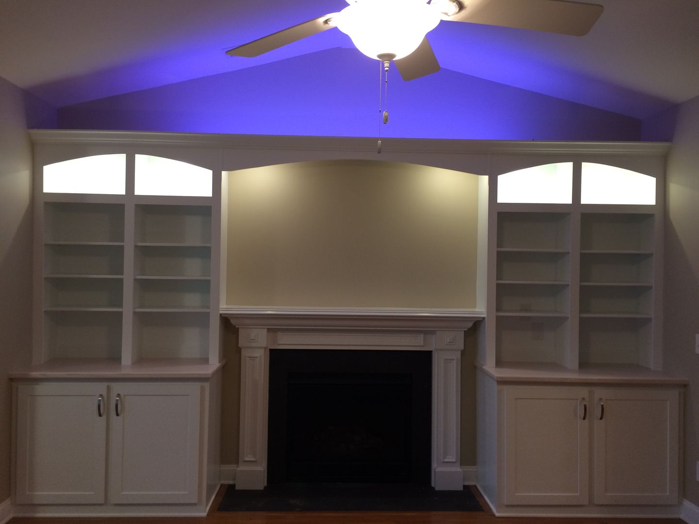 Built-in white bookshelves flank a fireplace, with cabinets below. Purple light shines above.