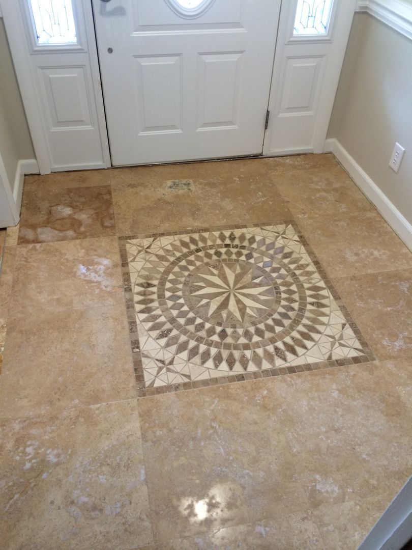Entryway with beige tile floor, decorative mosaic square, and white door.