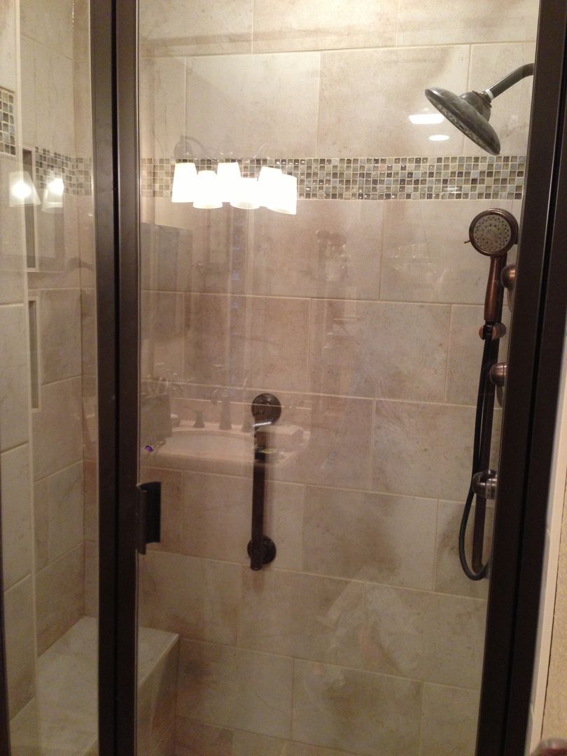 Shower stall with glass door, brown frame, tile walls, and hand shower.