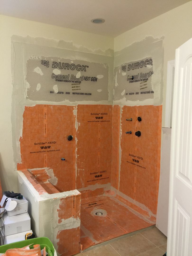 Shower stall under construction, orange waterproofing membrane on walls, white drywall, and a low curb.