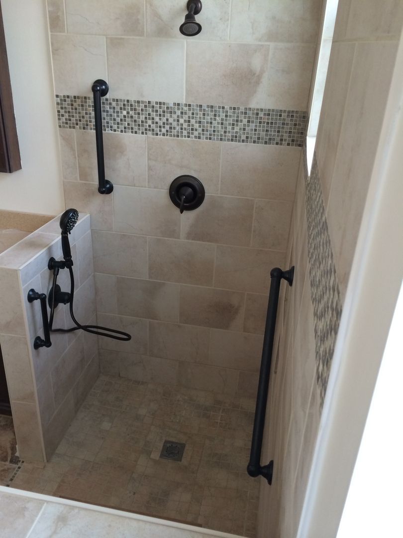 Accessible shower with dark fixtures and grab bars, beige tiles, and decorative mosaic accent.
