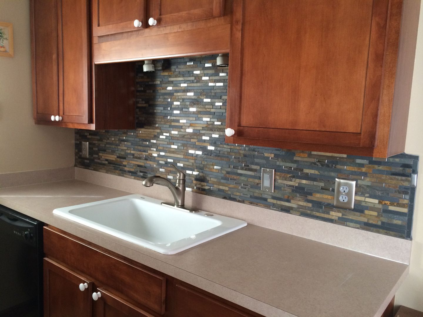 Kitchen with brown cabinets, white sink, beige countertop, and mosaic tile backsplash.