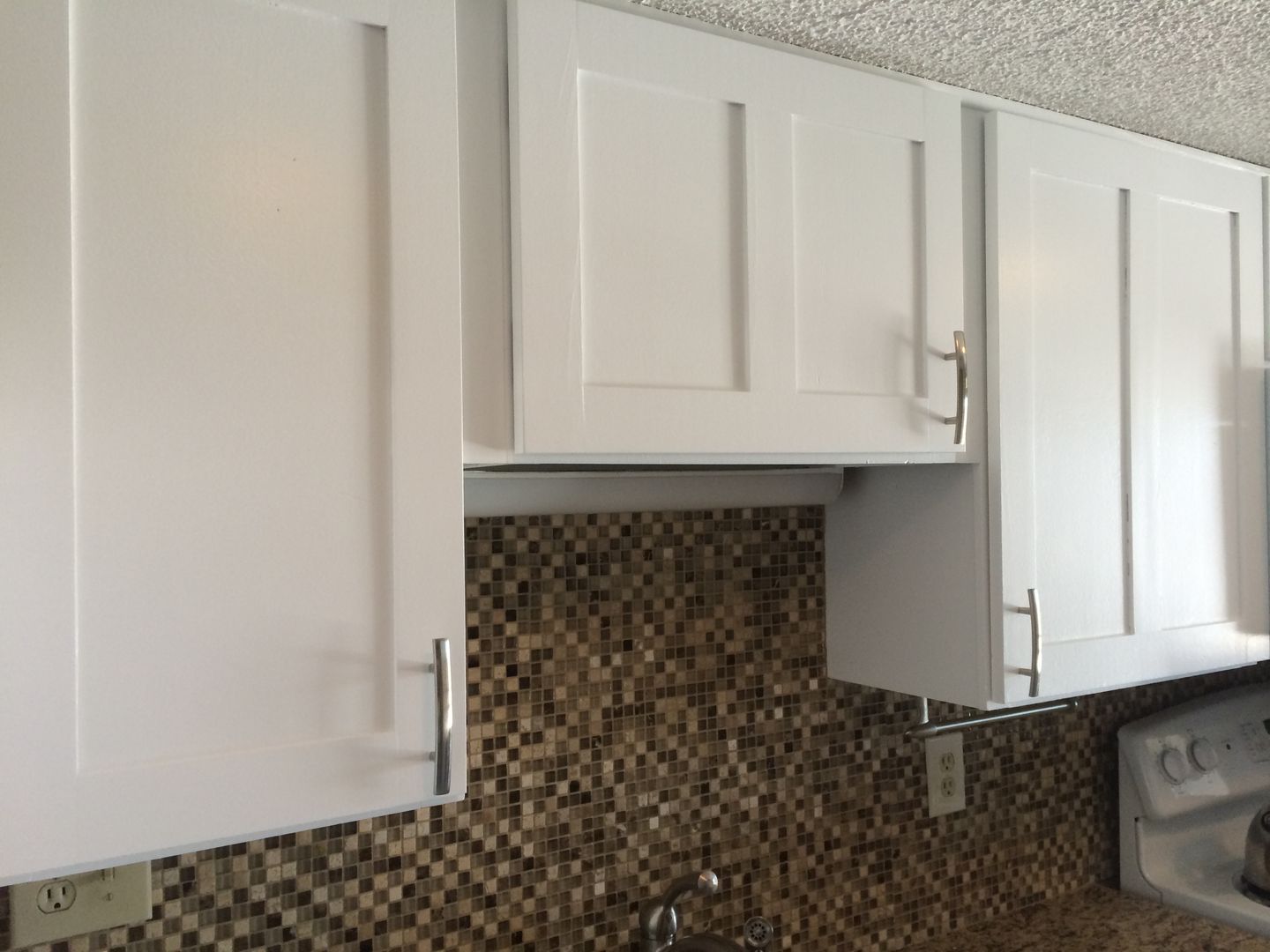 White kitchen cabinets with silver handles over a mosaic tile backsplash.
