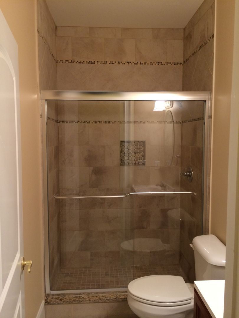 Shower stall with glass sliding doors, toilet, and tiled walls and floor.