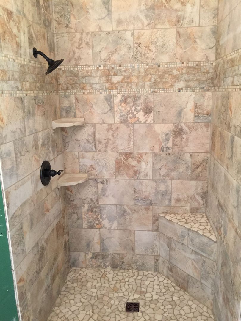 Shower with beige, brown, and white tile, pebble floor, built-in seat, and bronze shower fixtures.