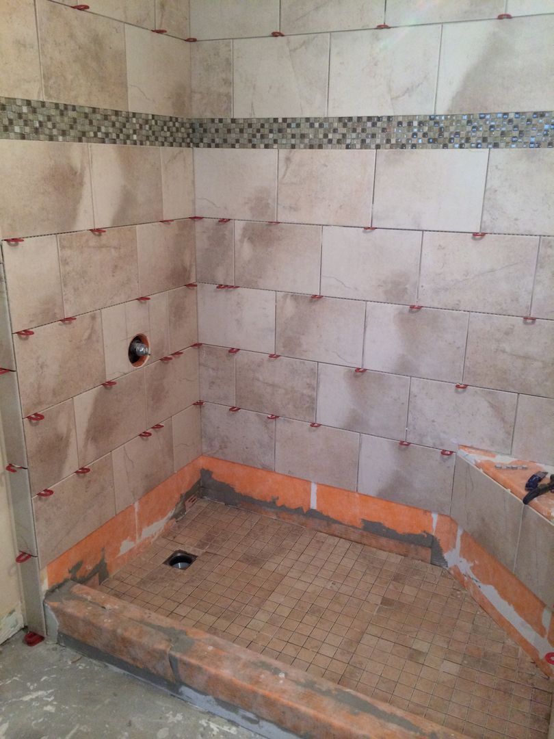 Shower with beige tile and mosaic accent, partially tiled. Red tile leveling system visible.