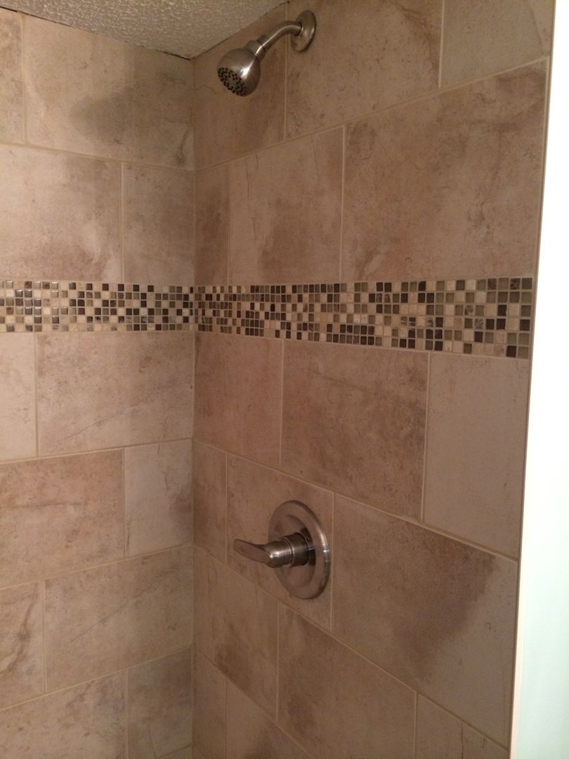 Shower stall with beige tile, mosaic tile accent, and silver fixtures.