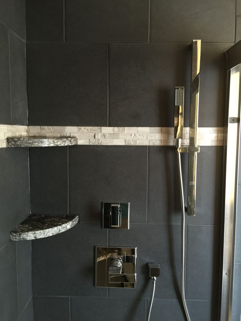 Dark gray tiled shower with a decorative shelf, shower controls, and a handheld showerhead.