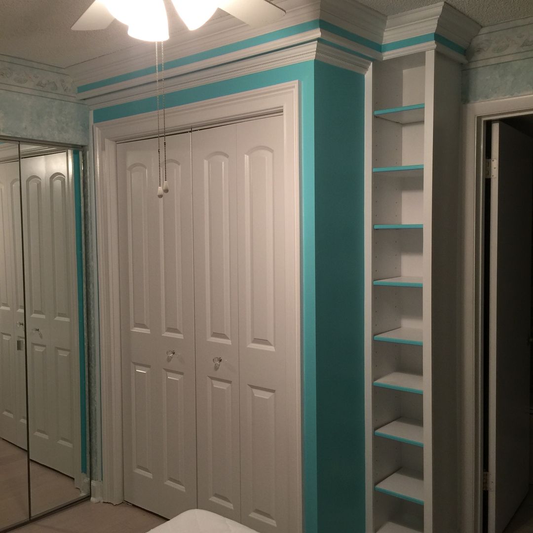 Bedroom with white closet doors, turquoise trim, and built-in white shelves.