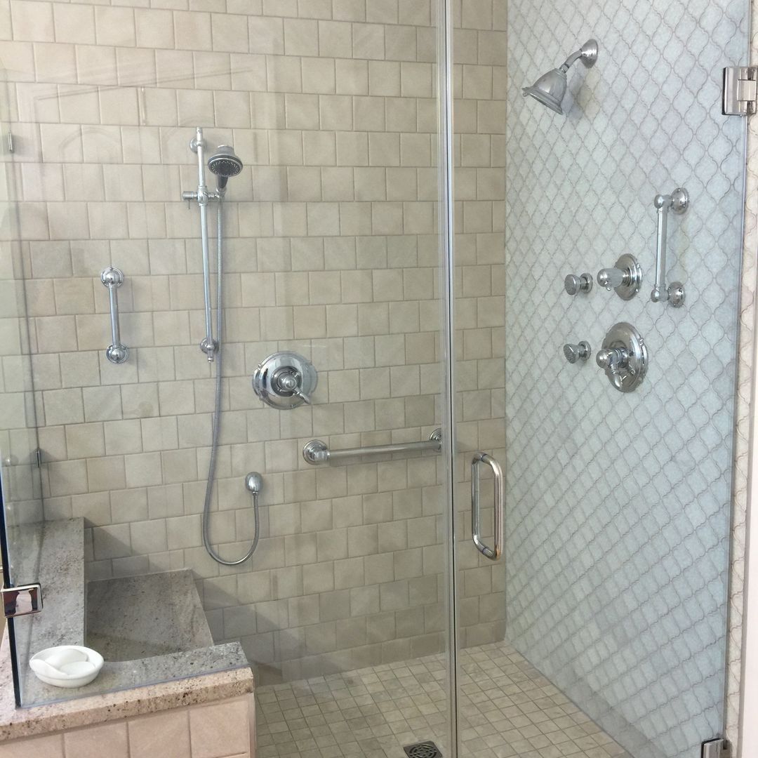 Shower with glass door, multiple showerheads, and tiled walls.