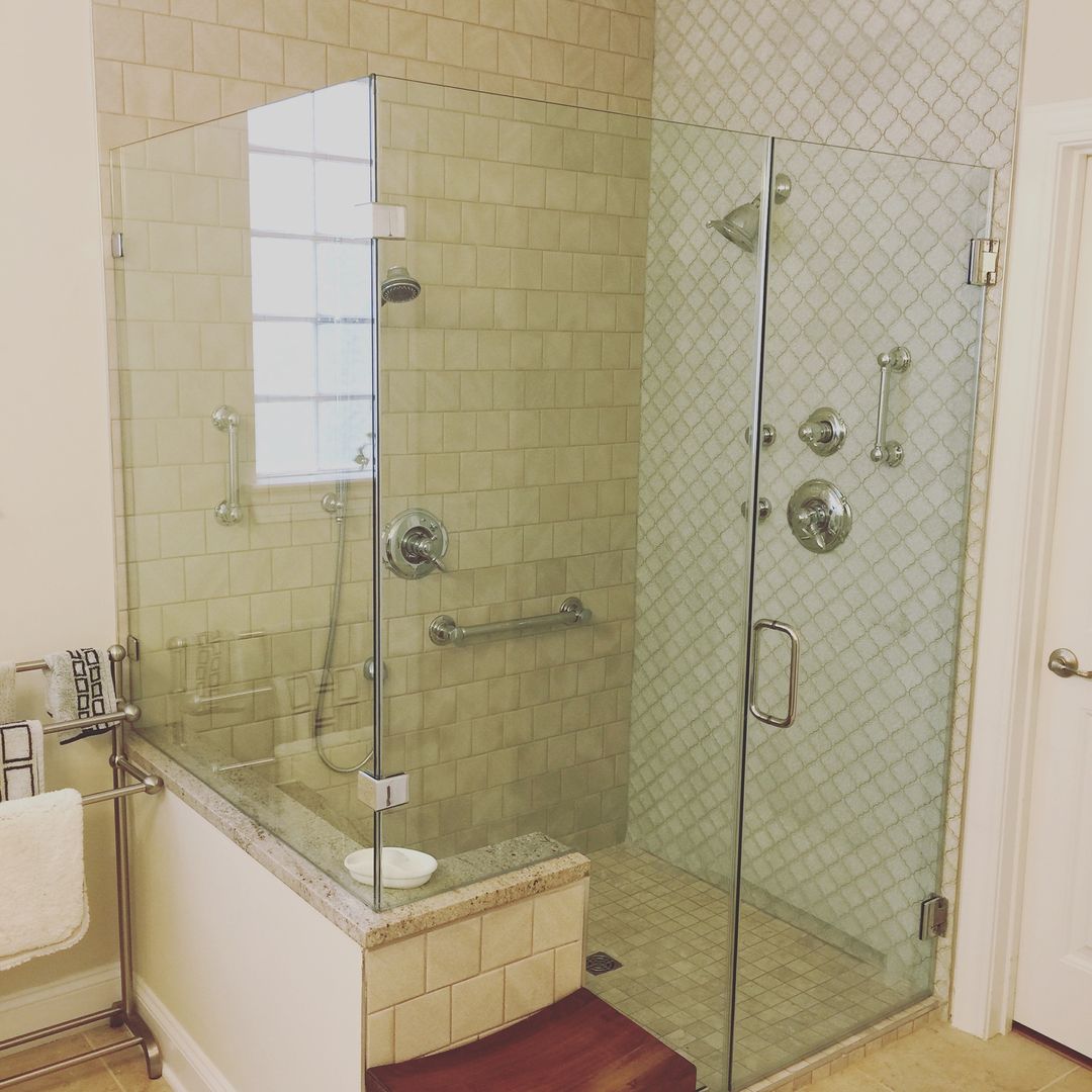 Glass-enclosed shower in a tiled bathroom with a grab bar, showerheads, and a built-in bench.