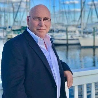 A man in a suit and glasses is leaning on a railing next to a body of water.