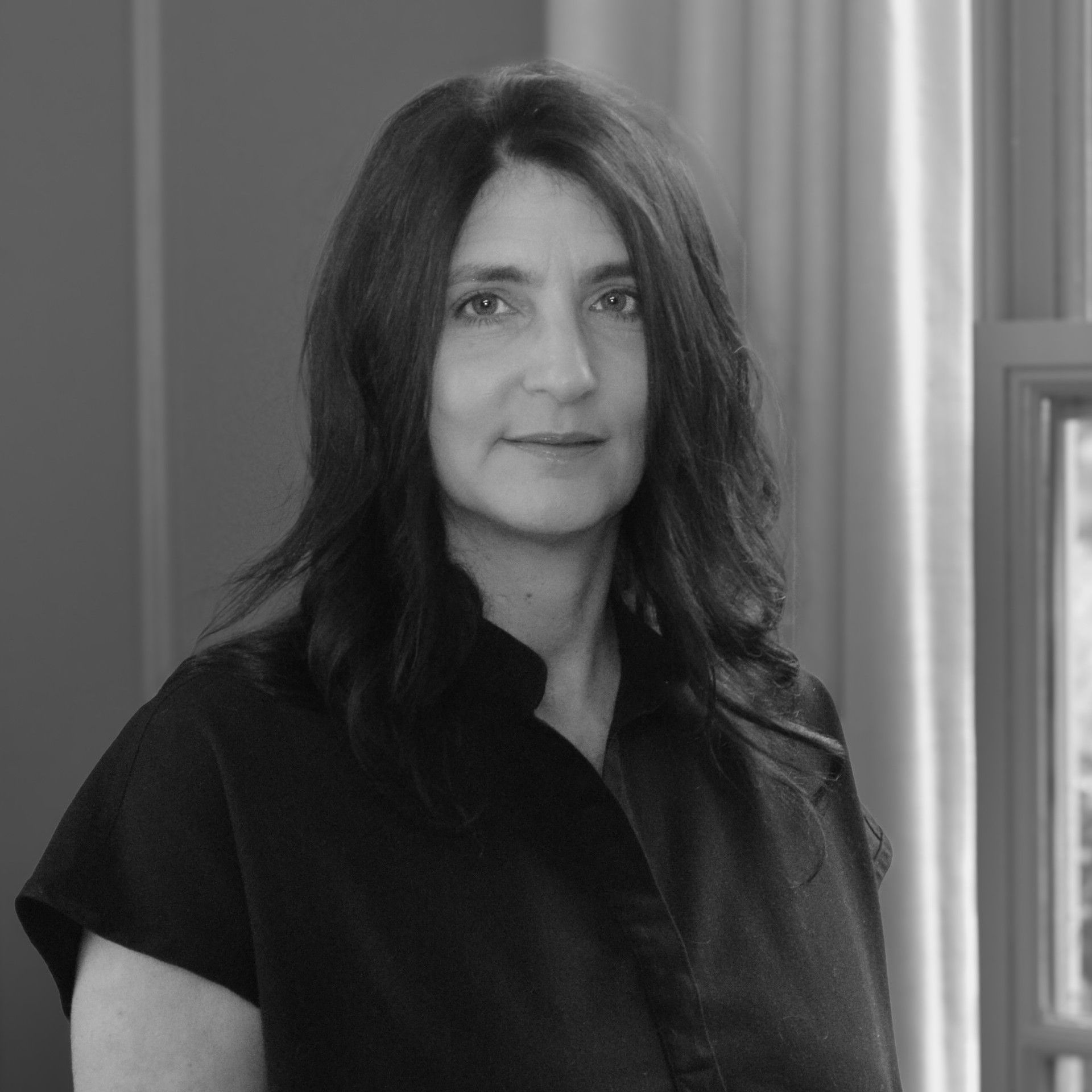 A woman in a black shirt is standing in front of trees.