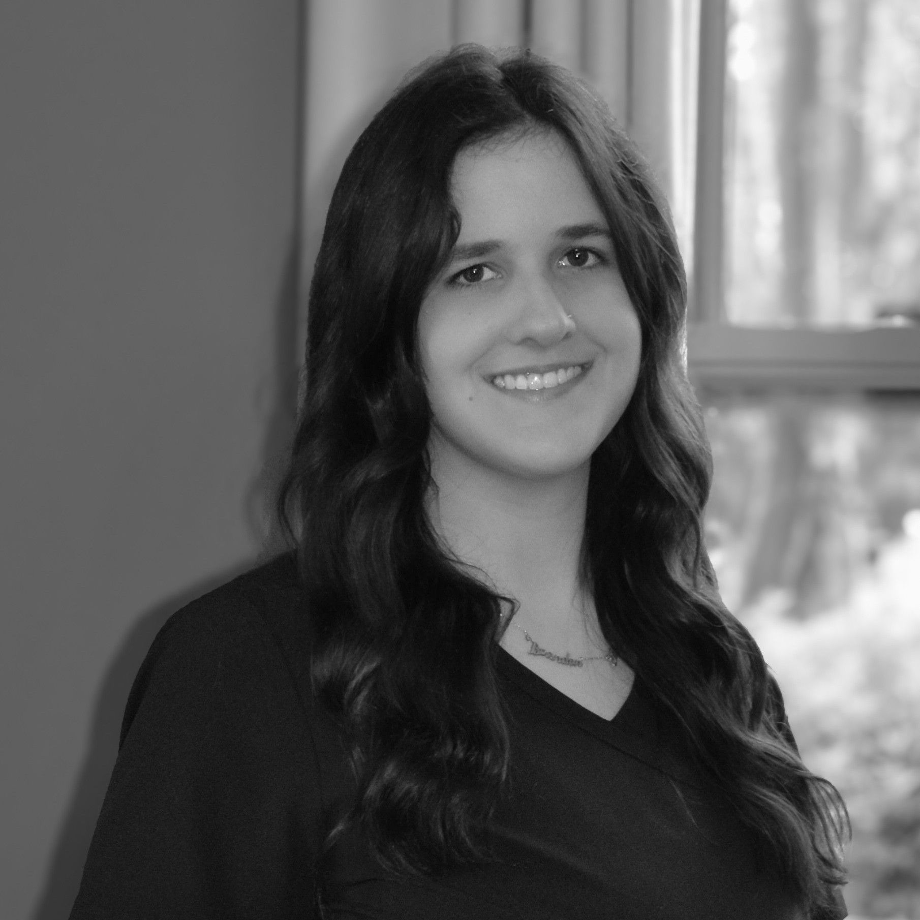 A black and white photo of a woman smiling in front of a window.