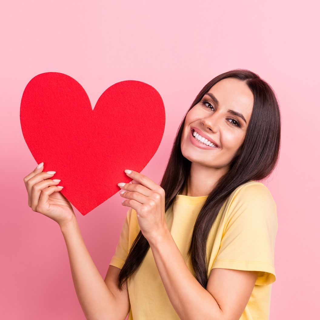 A woman is holding a red heart in her hands and smiling.