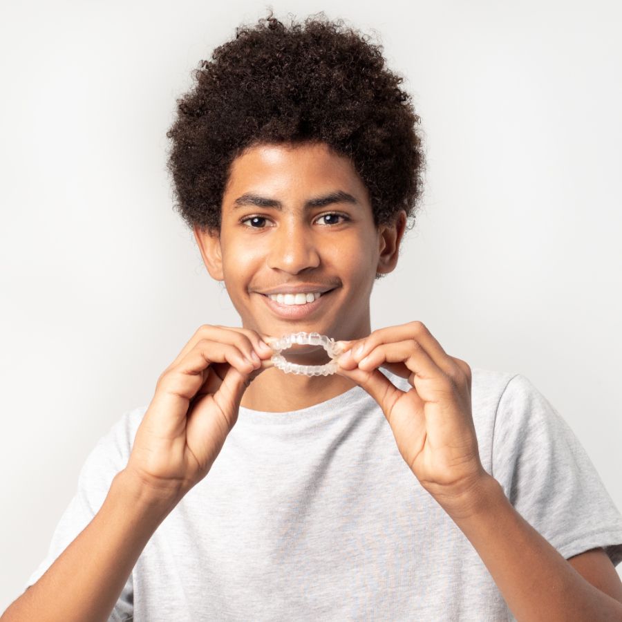 A young man is holding a clear retainer in his hands and smiling.