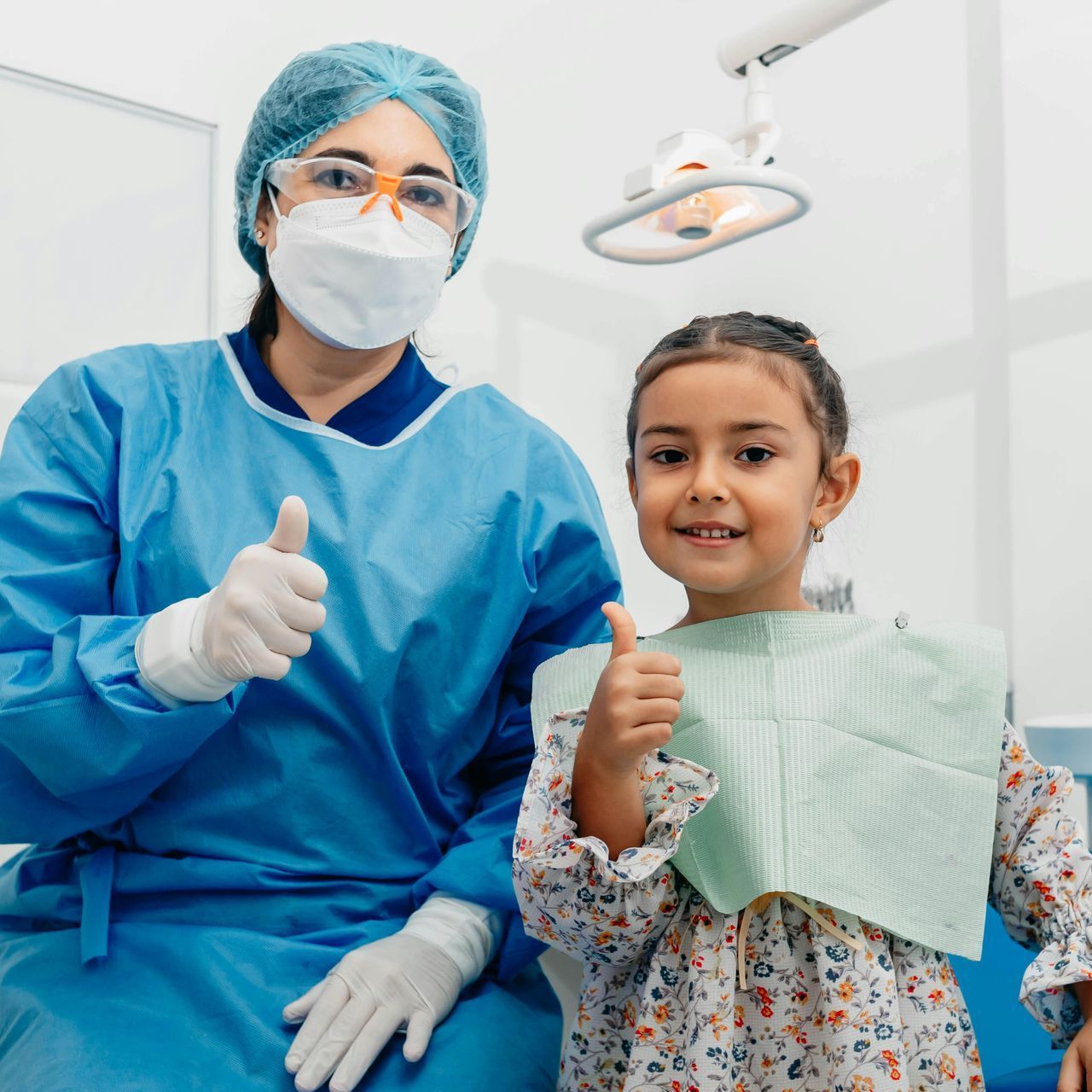 A dentist and a little girl are giving a thumbs up in a dental office.