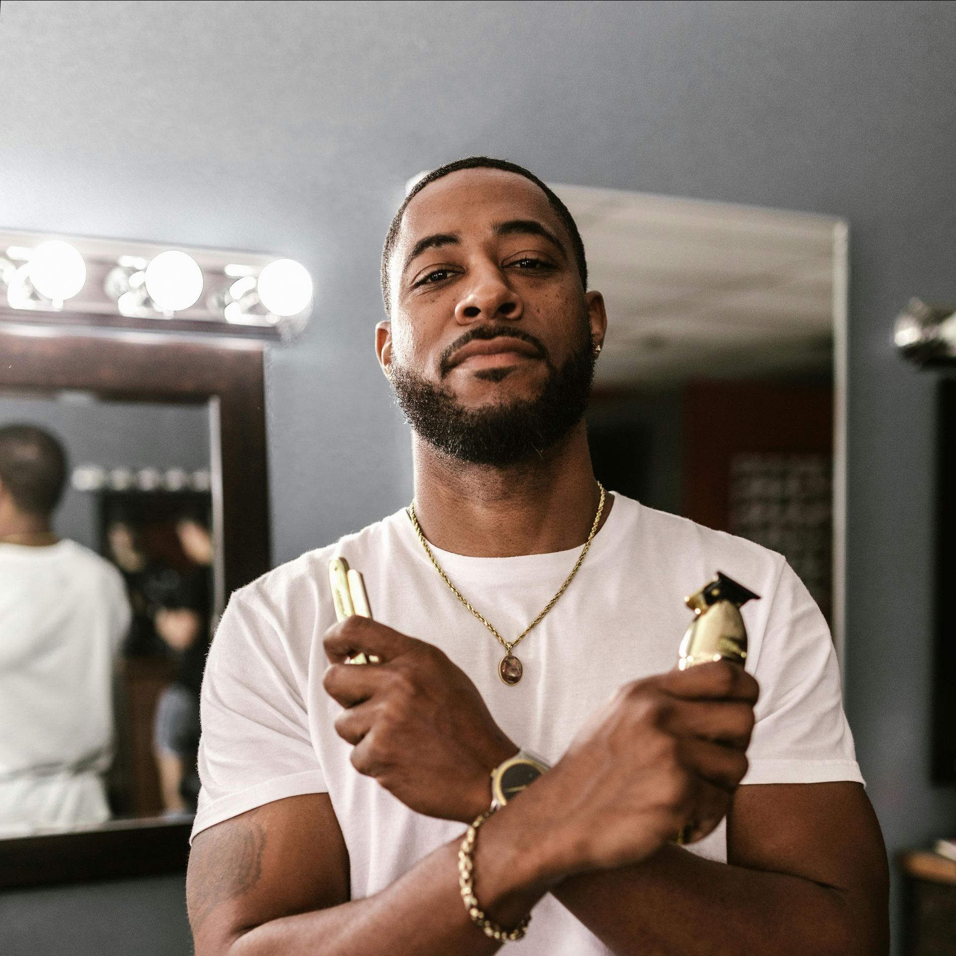 A man in a white shirt and beard is holding a hair clipper in front of a mirror.