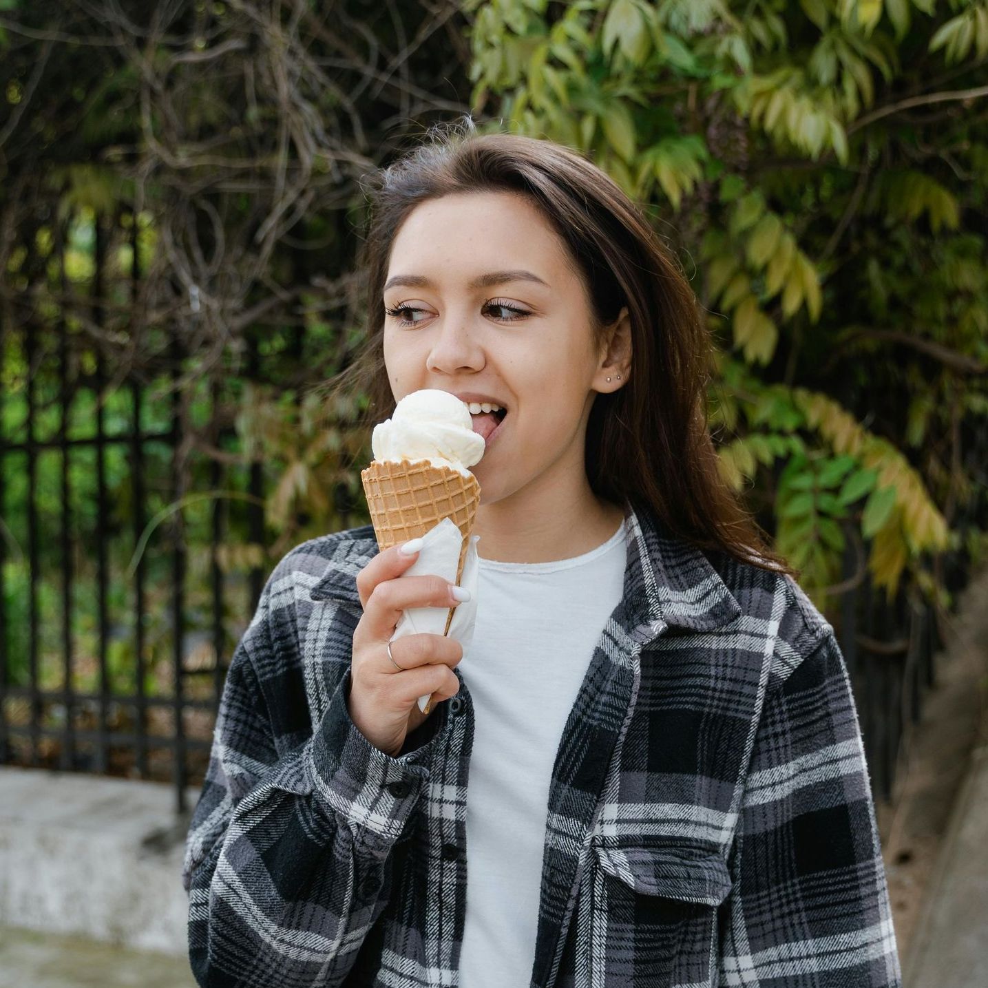 A woman in a plaid shirt is eating an ice cream cone.