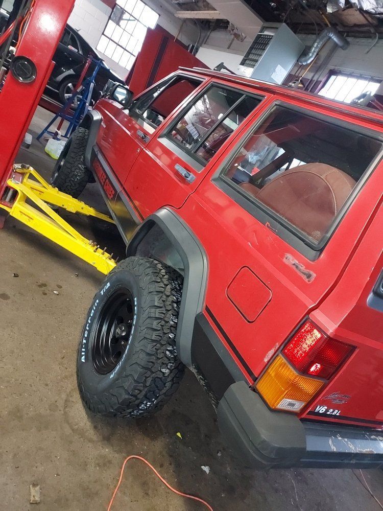 a red jeep is sitting on a lift in an auto repair shop