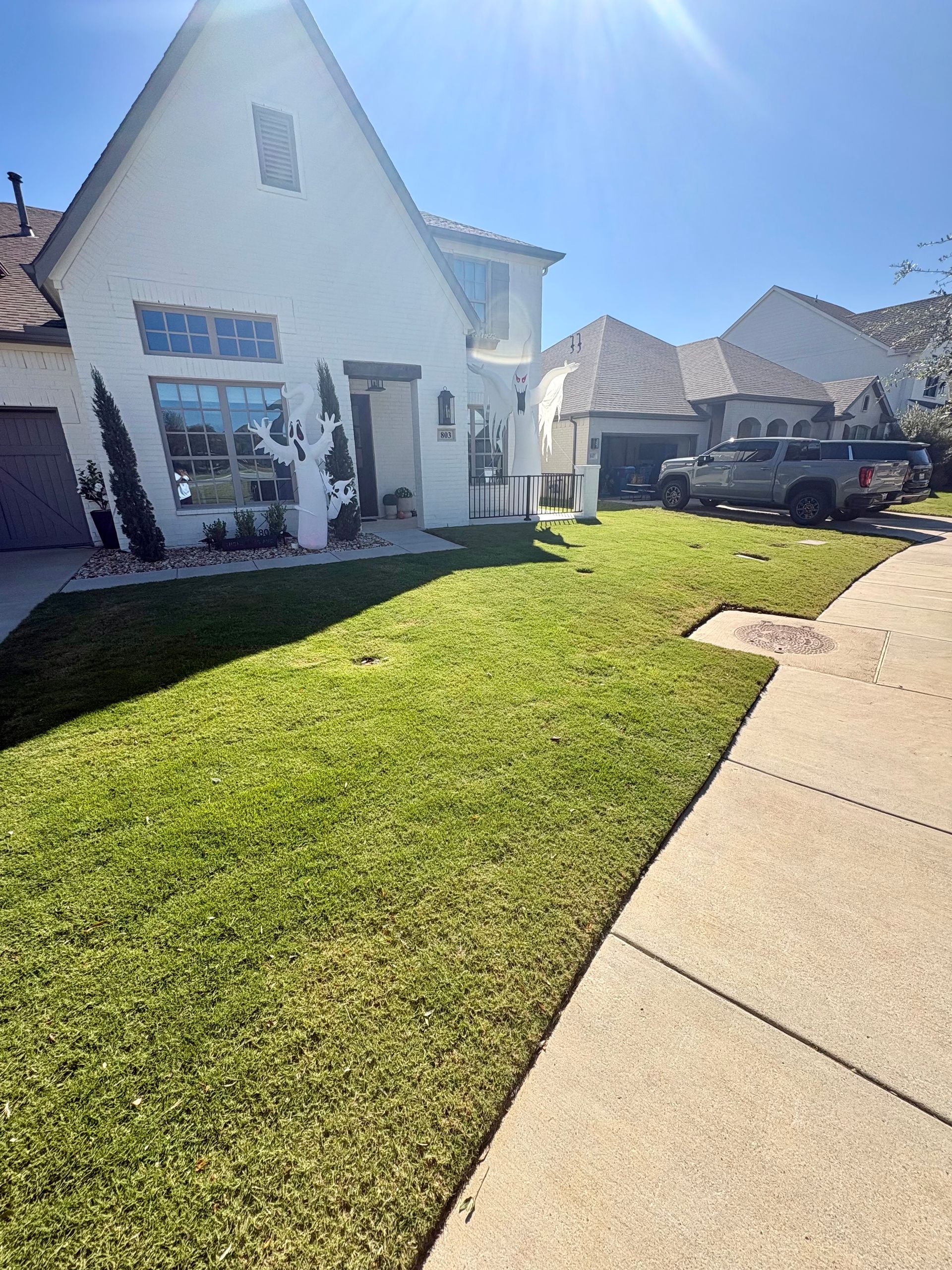 A white suburban house with a green lawn and concrete driveway under a clear blue sky.