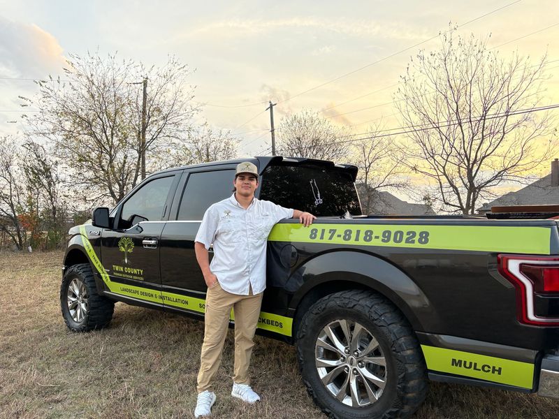 A person stands beside a black pickup truck with green graphics, including a phone number and the word
