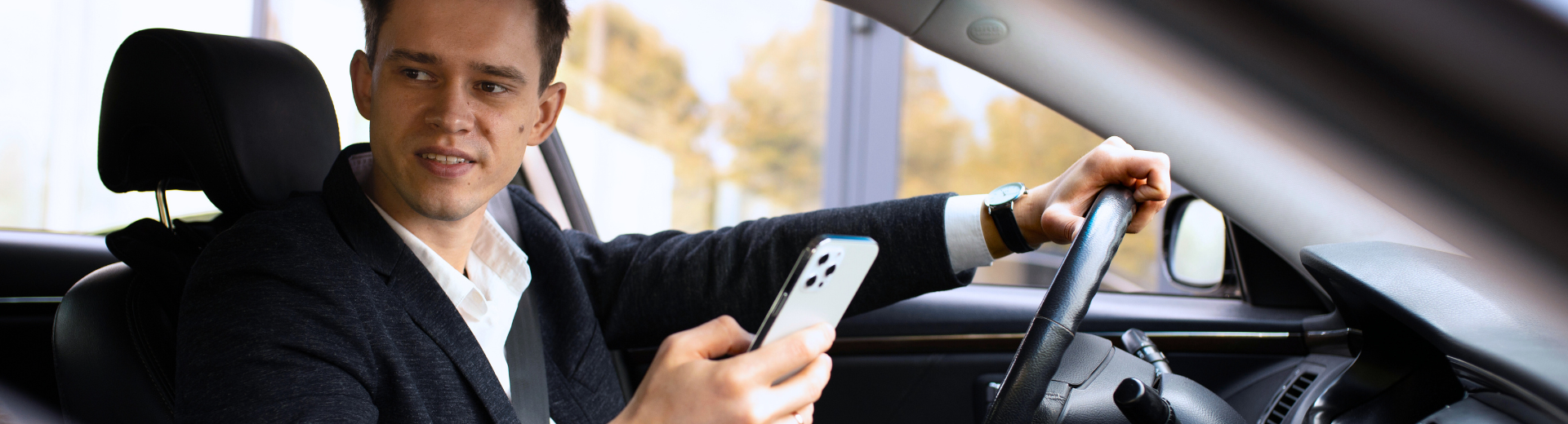 Um homem está sentado no banco do motorista de um carro segurando um telefone celular.