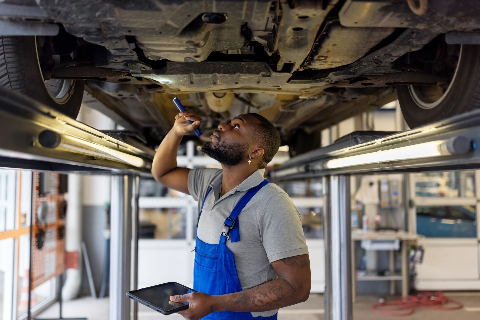 A mechanic examining brake pads of a lifted car during an inspection, at an auto repair shop. A mechanic examining brake pads of a lifted car during an inspection, at an auto repair shop.