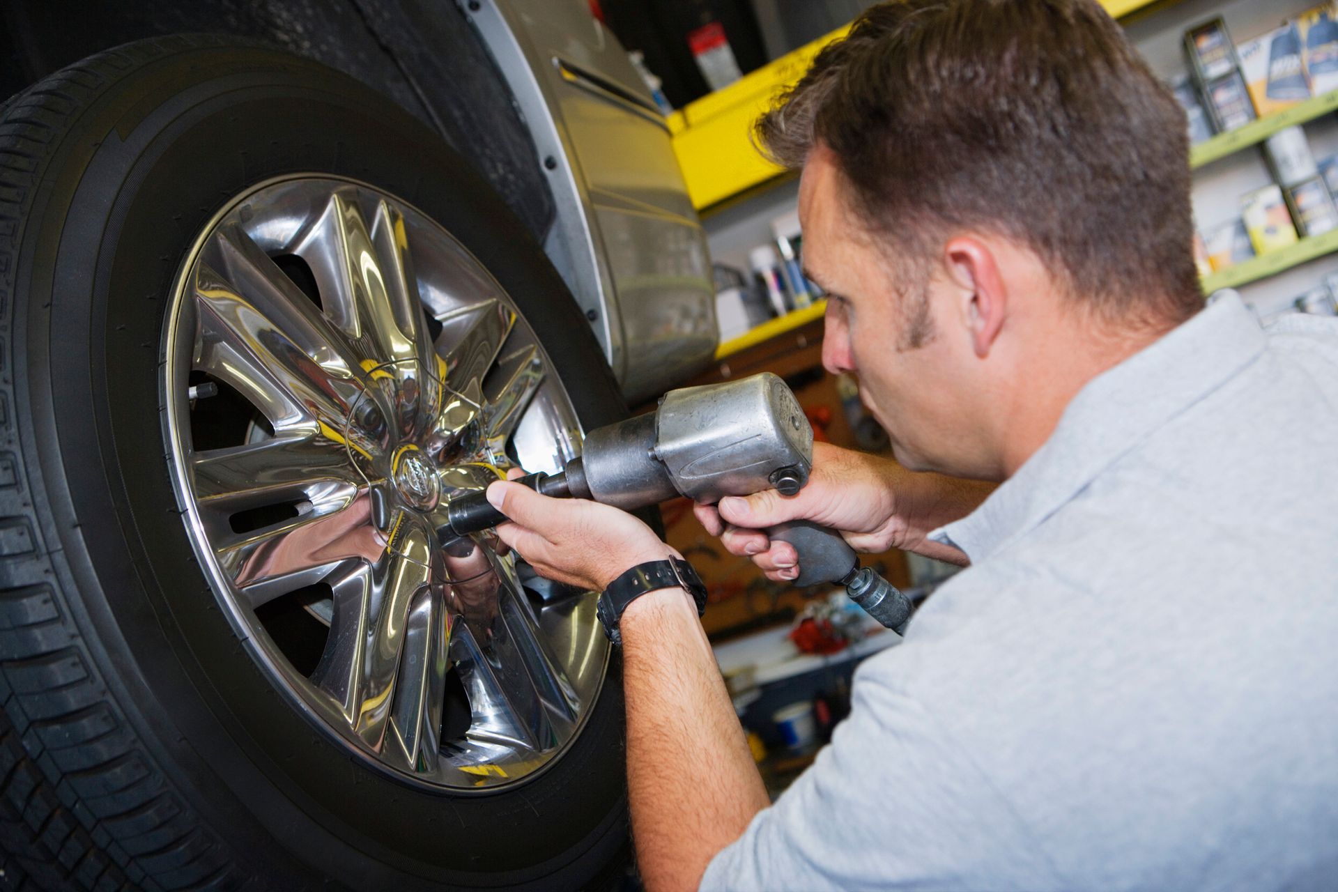Auto technician using impact wrench to tighten car wheel lug nuts in automotive repair shop.