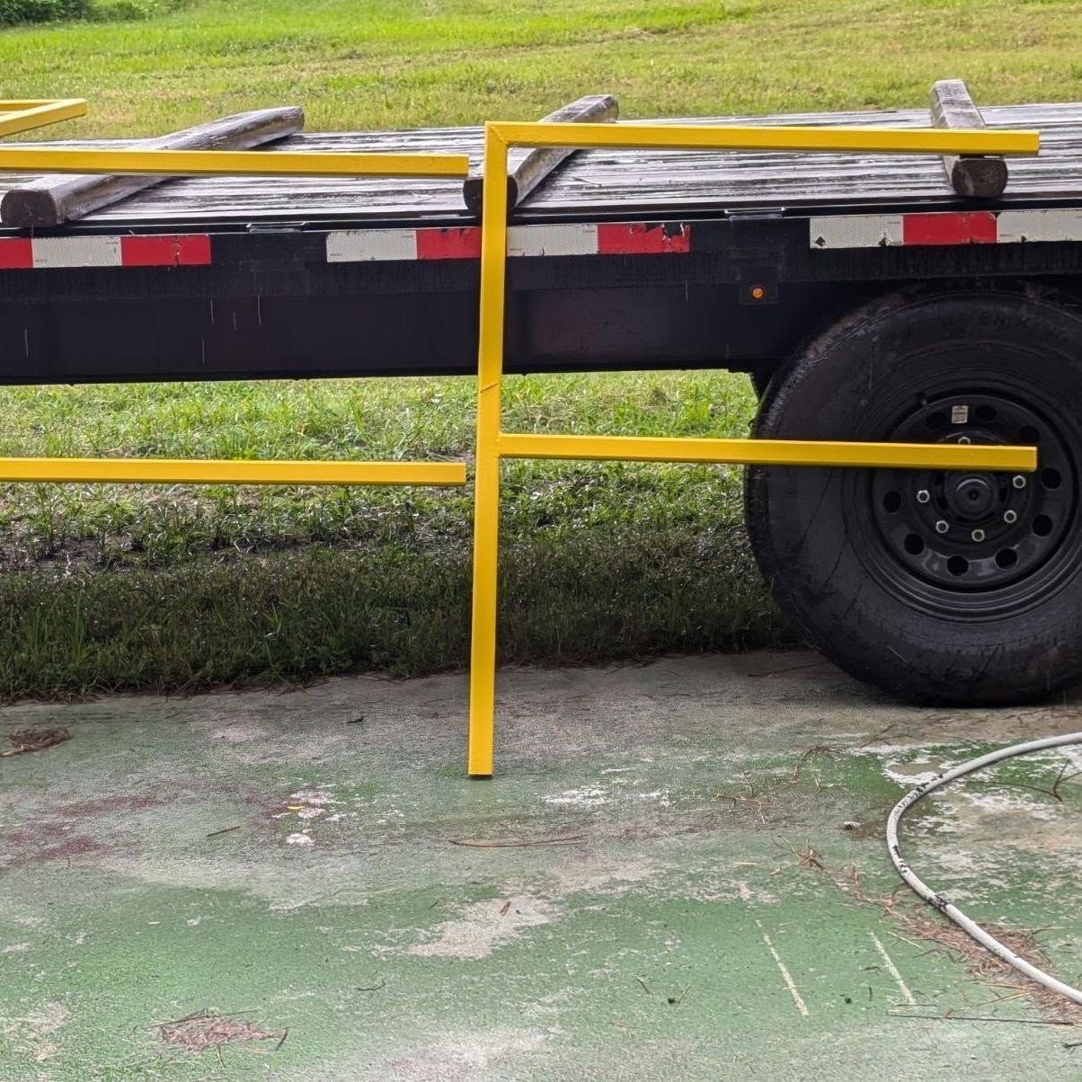 Yellow metal safety rail on a black trailer, parked on concrete near grass.