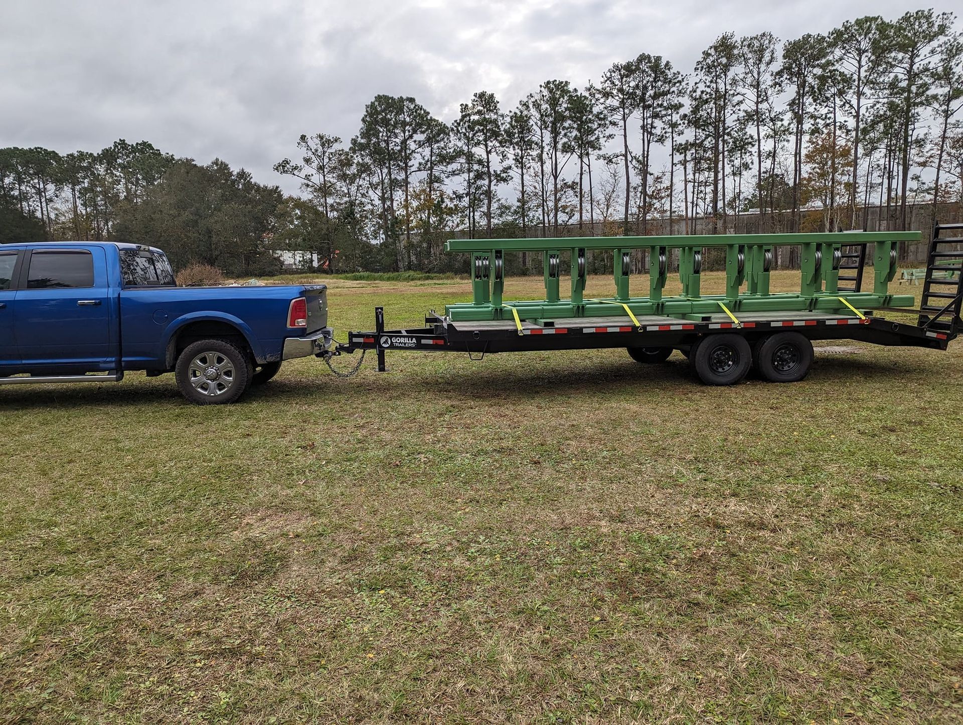 Blue pickup truck towing a trailer with a green ladder-like structure on a grassy field.