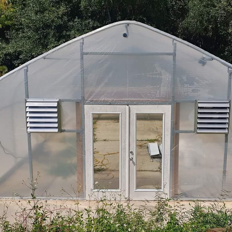 Greenhouse with clear plastic walls, double doors, and vents.