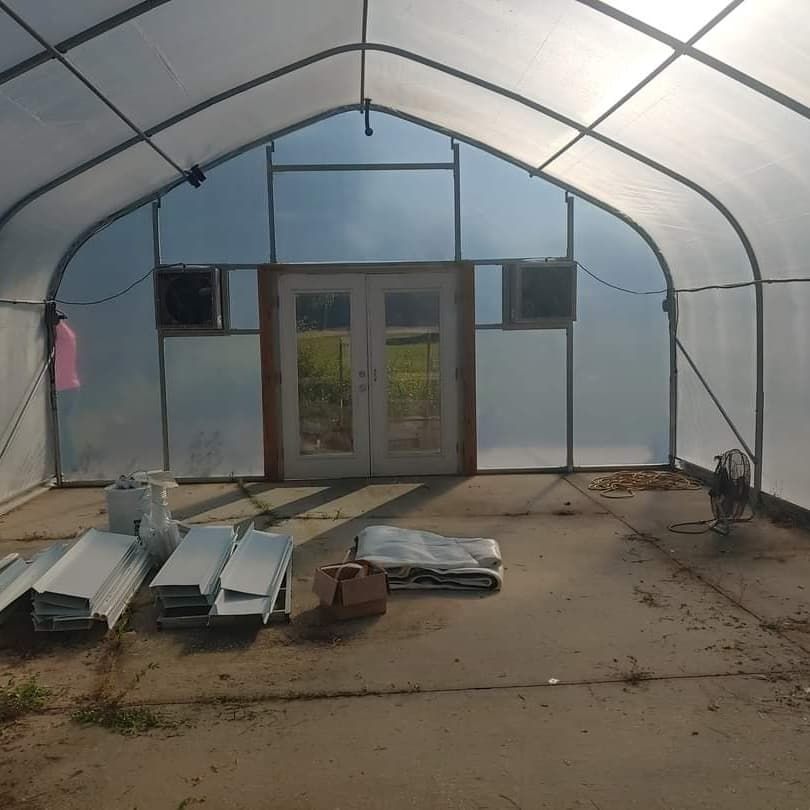 Inside a greenhouse, concrete floor, double doors, two fans.