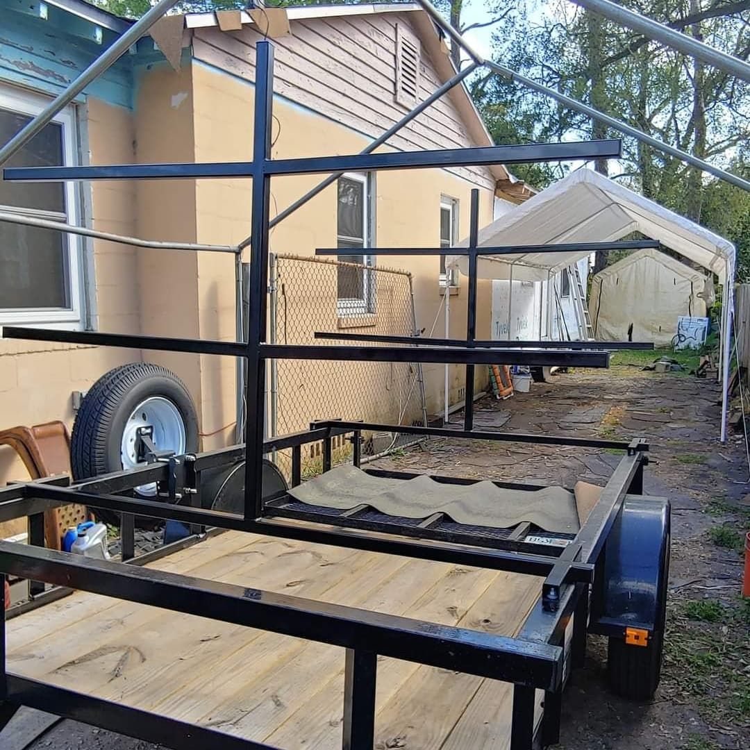 Black trailer with a black metal frame attached, in front of a tan house.