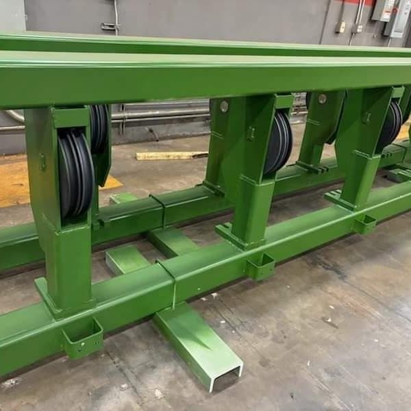 Green metal conveyor track with black pulleys, in an industrial setting.