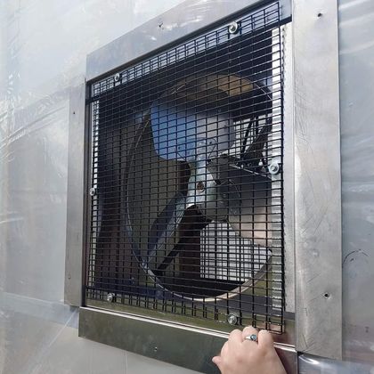 A large ventilation fan covered with a metal grid. Hand reaches toward it.