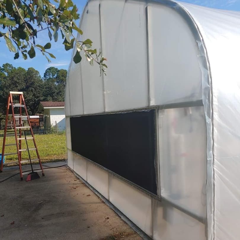 Greenhouse with a black shade cloth in a side opening. A ladder leans against the side.