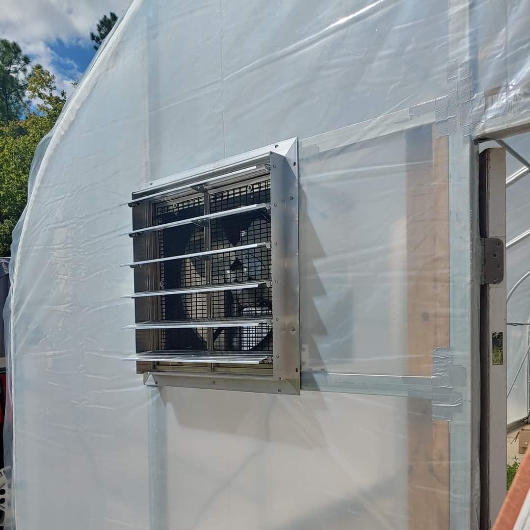 Exterior of a greenhouse, with an exhaust fan installed in the translucent plastic side.