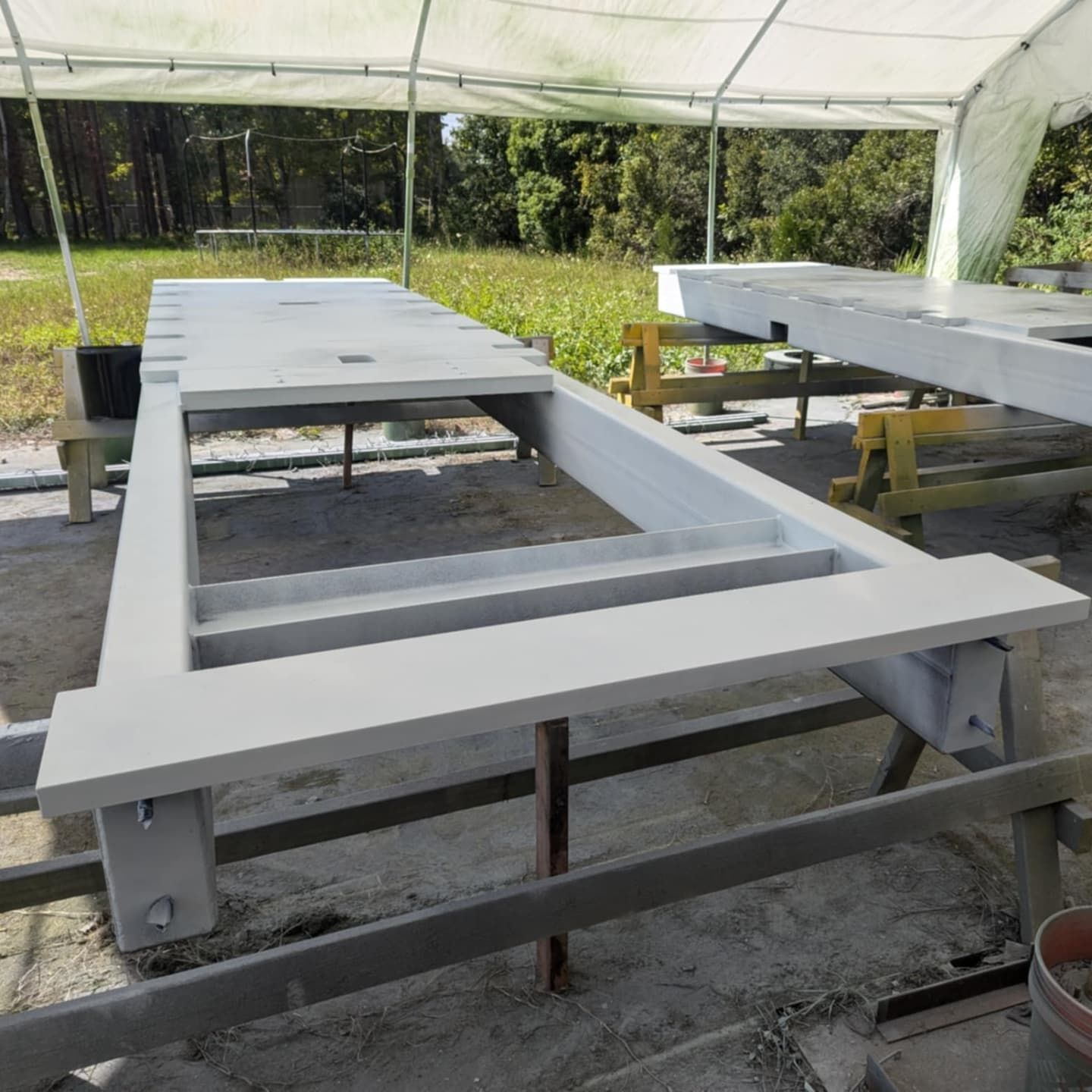 Concrete rectangular frame on supports outdoors under a white tarp.