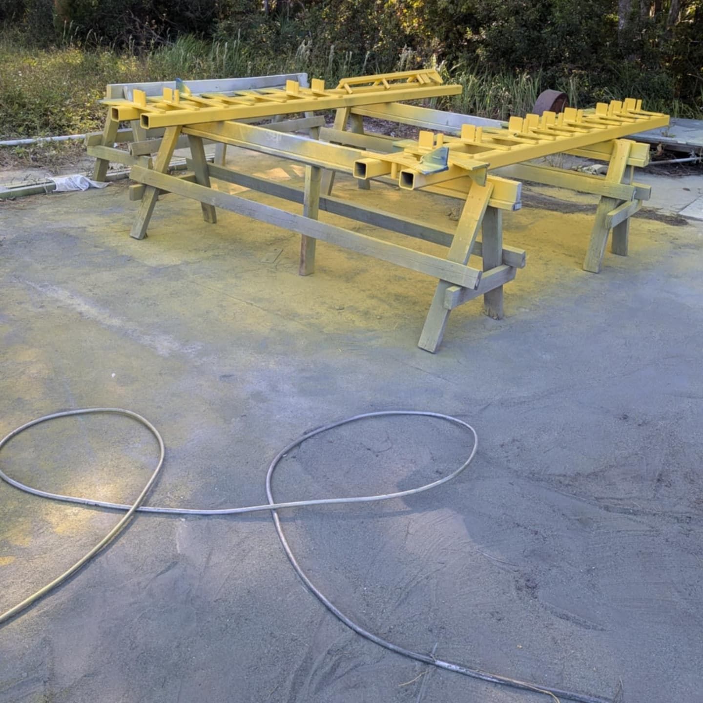 Two yellow painted metal structures on sawhorses outside, hose coiled in foreground.