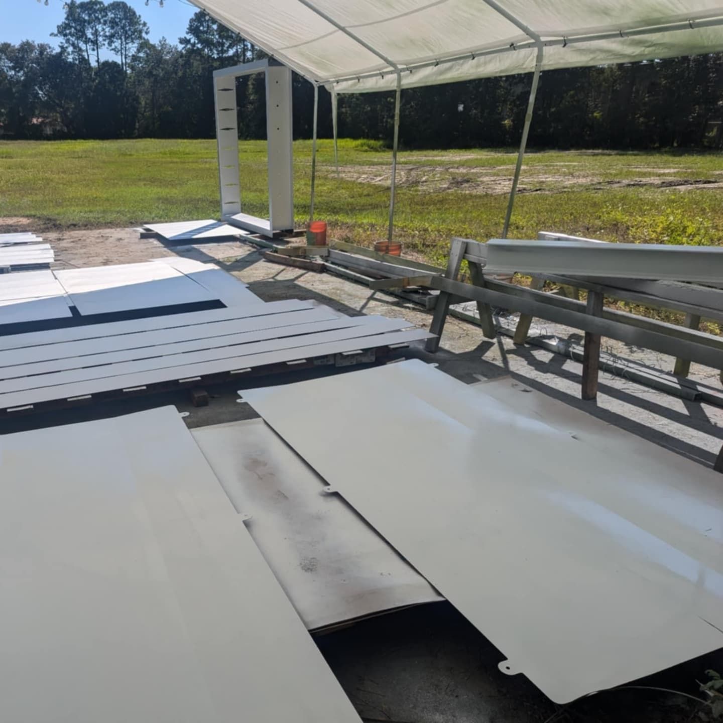 White painted metal sheets and frame under a canopy, outdoors on a sunny day.