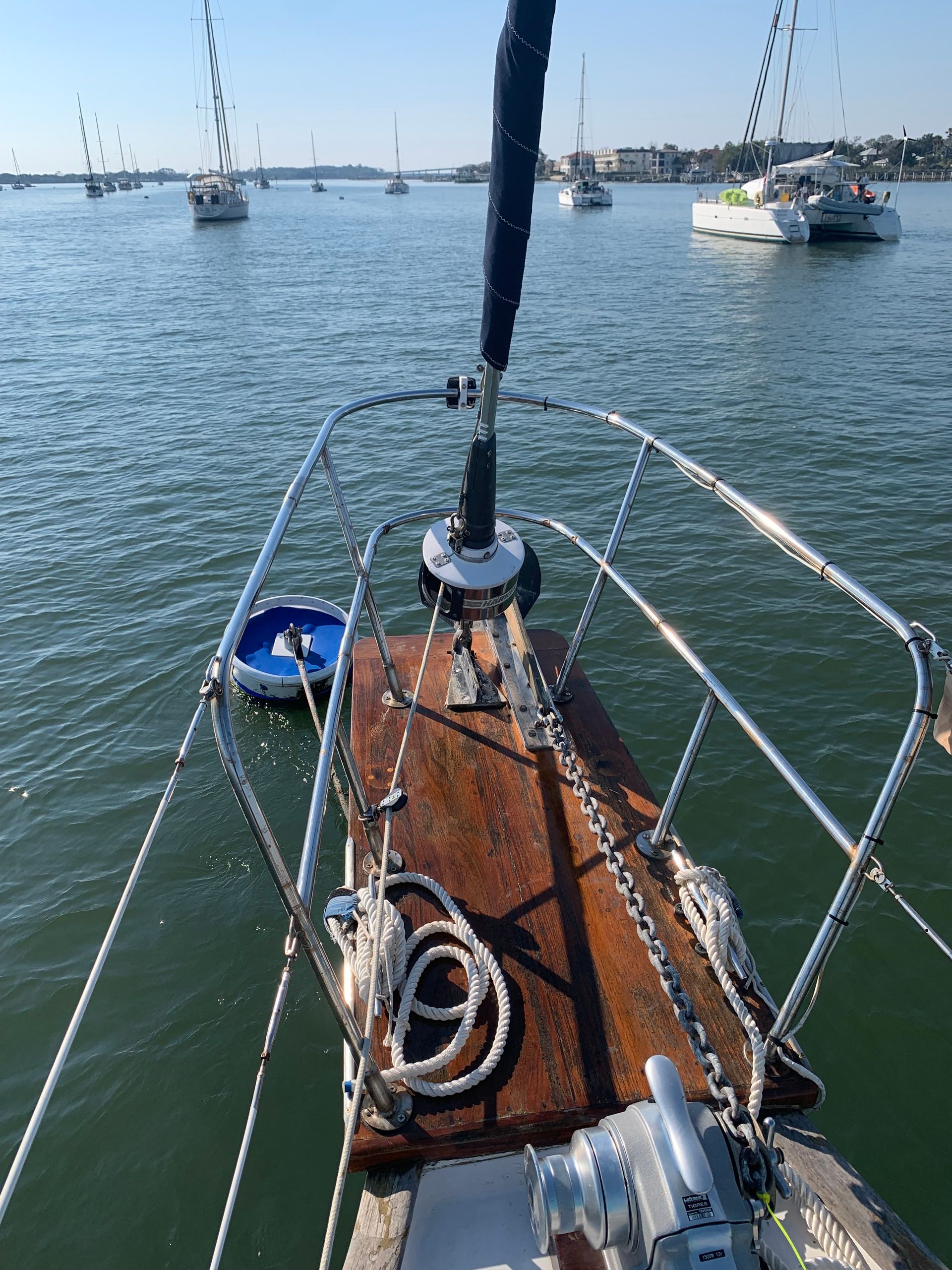 Bow of a sailboat on water, other boats in the distance, sunny day.