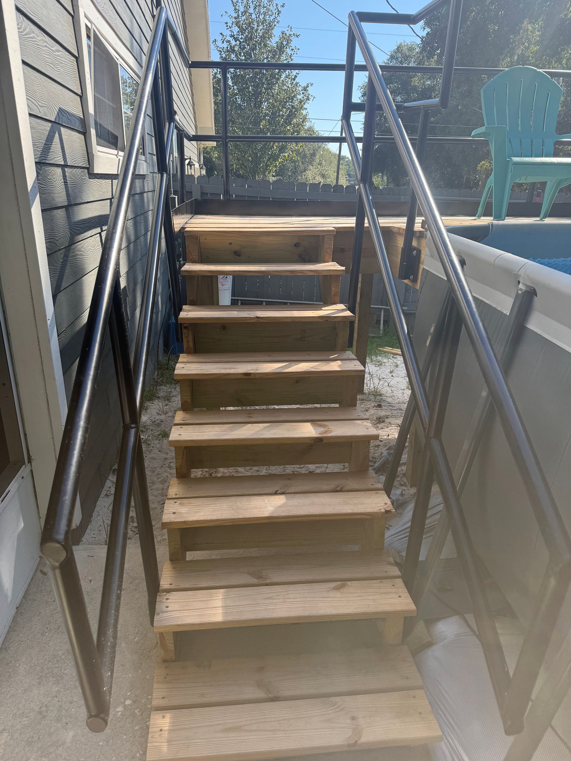Wooden outdoor staircase with black metal railings leading up to a pool.