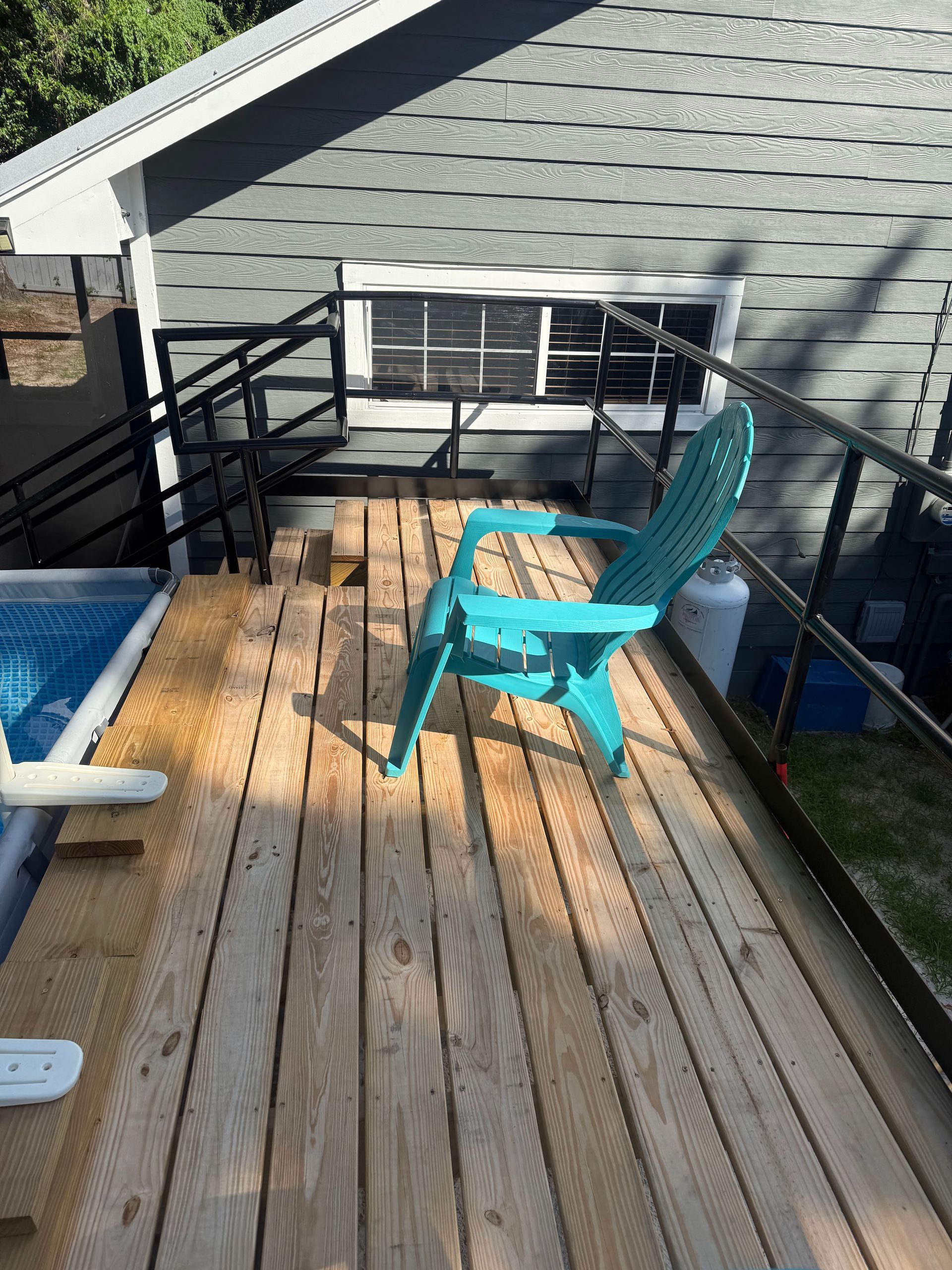 Wooden deck with a blue chair, railing, and hot tub beside a gray building.
