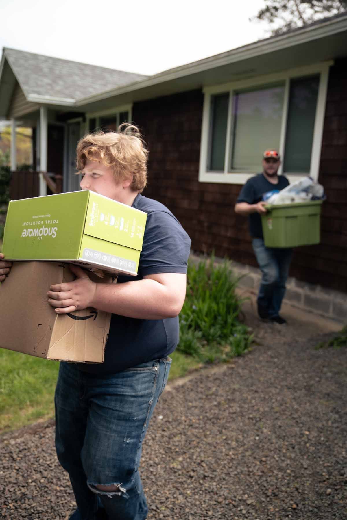 Two men are carrying boxes into a house.