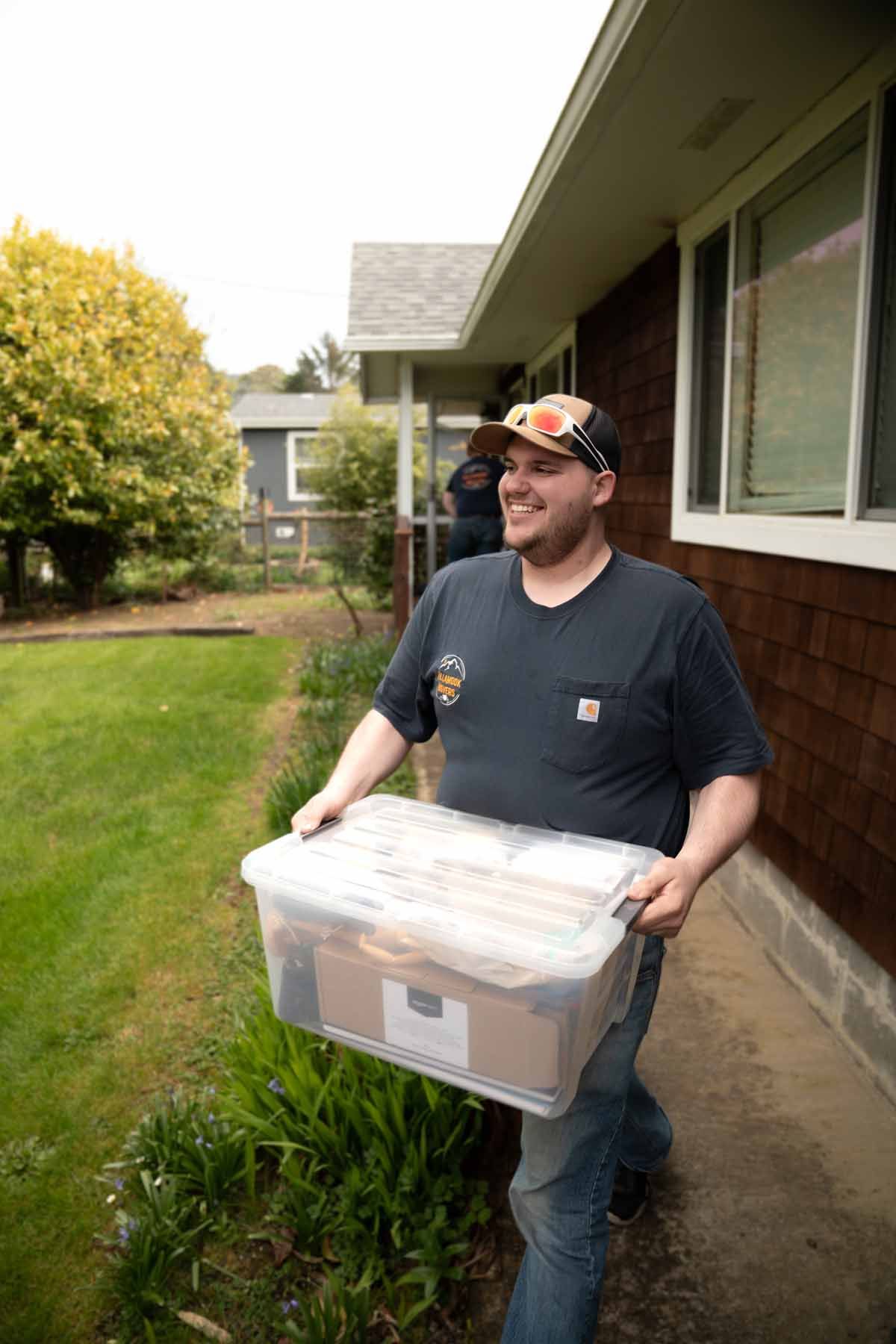A man is carrying a plastic container in front of a house.