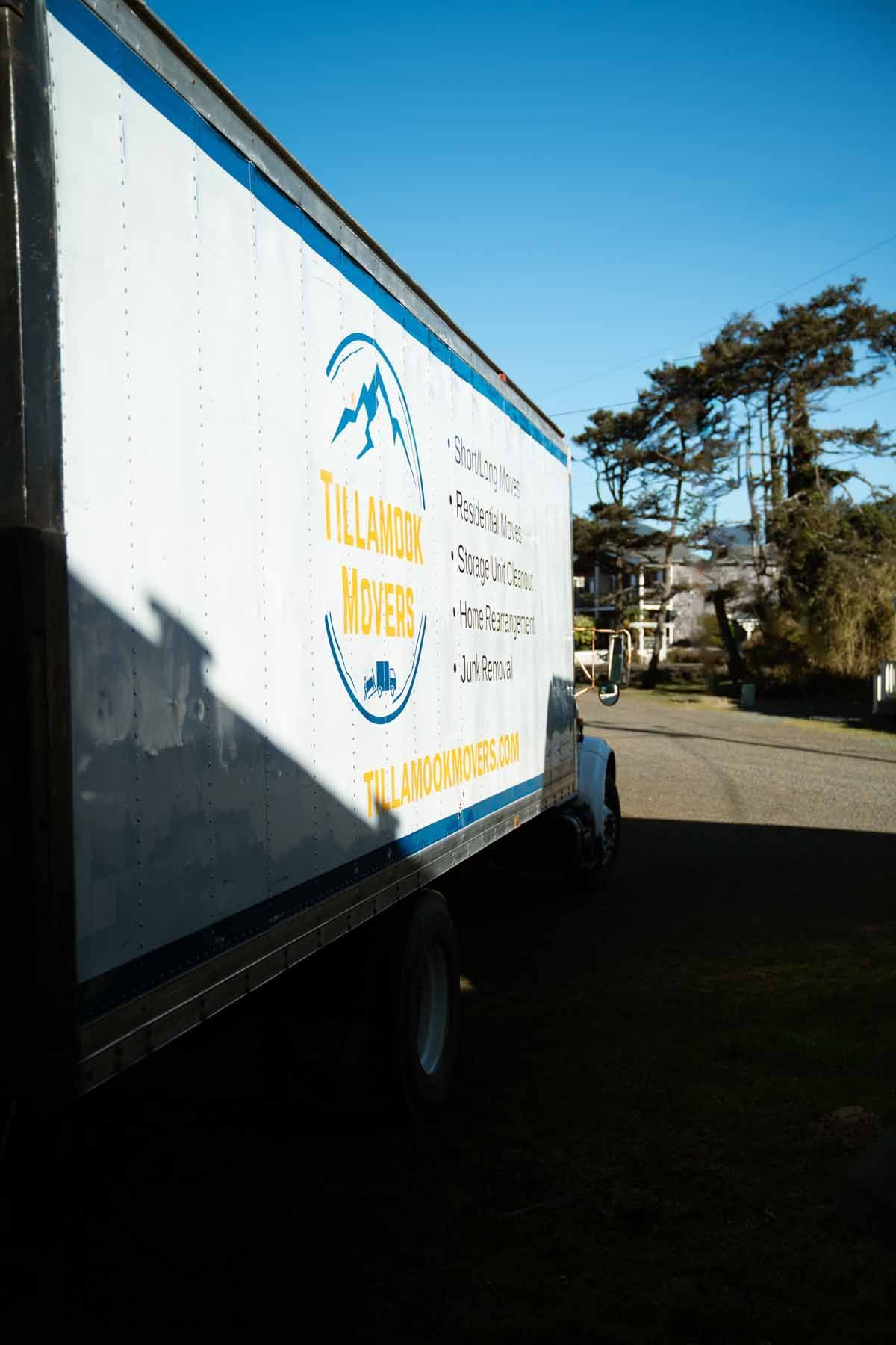 A white and blue moving truck is parked on the side of the road.