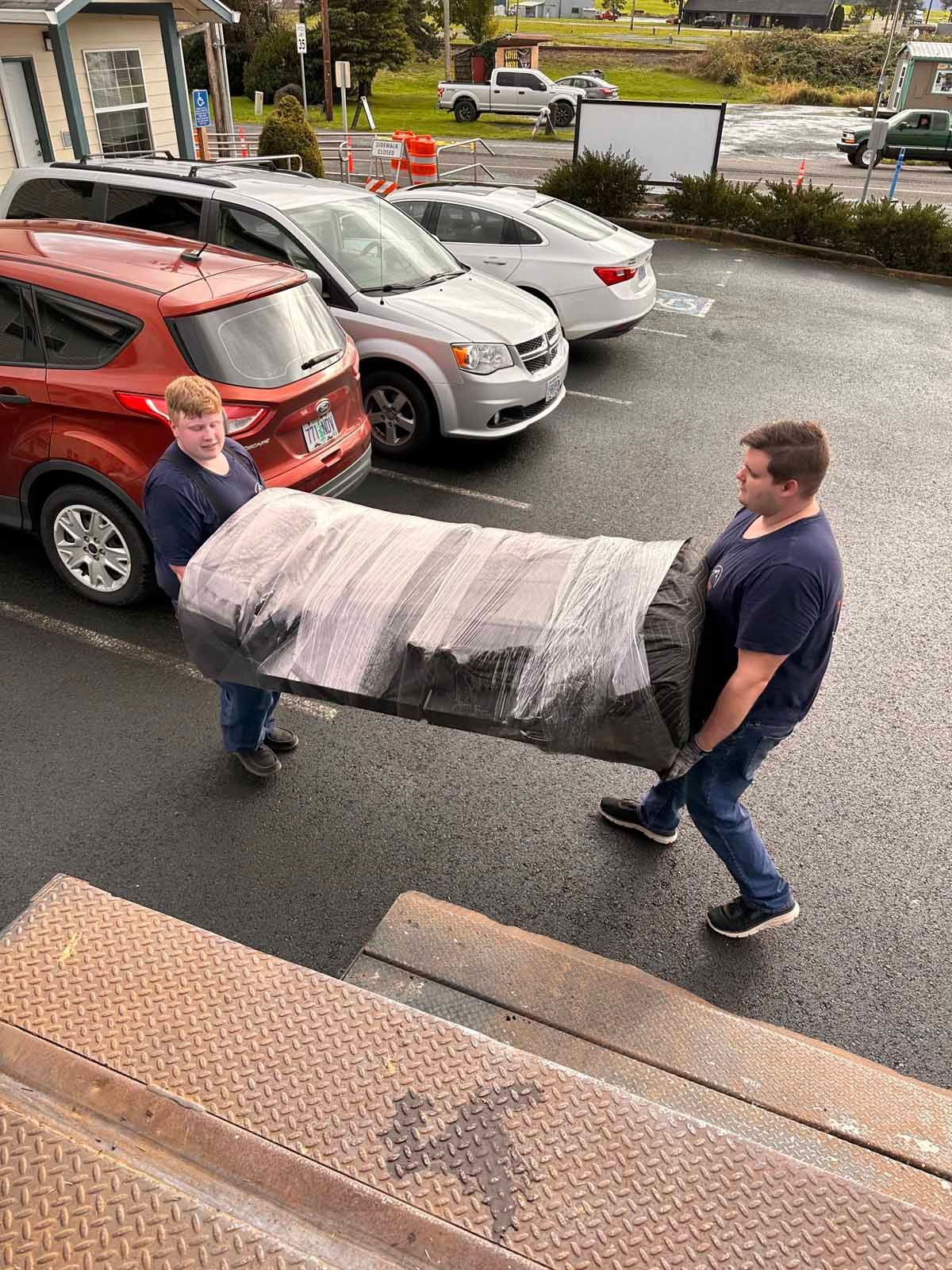 Two men are carrying a large piece of furniture in a parking lot.